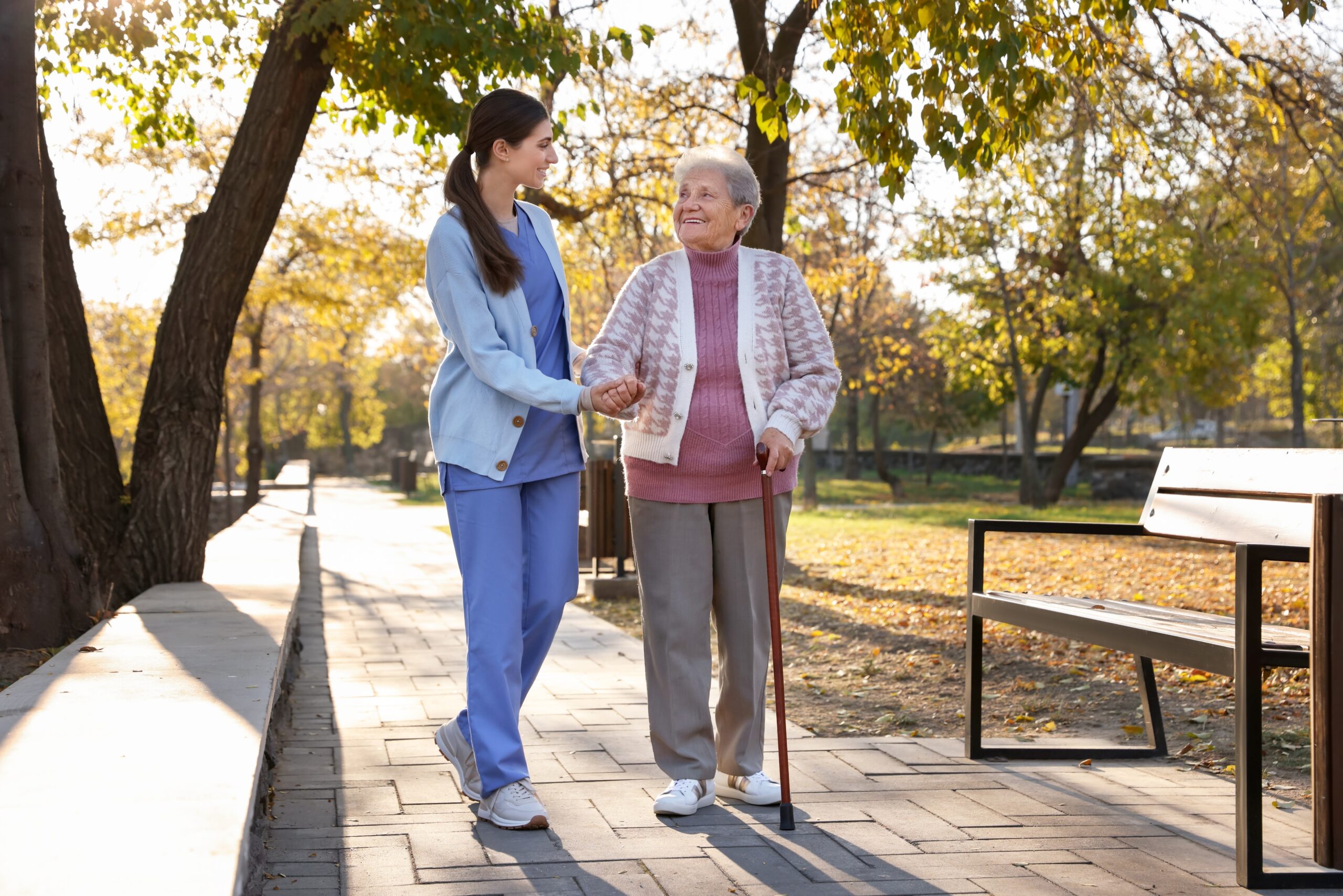 Elderly,Woman,With,Walking,Cane,And,Her,Caregiver,In,Park